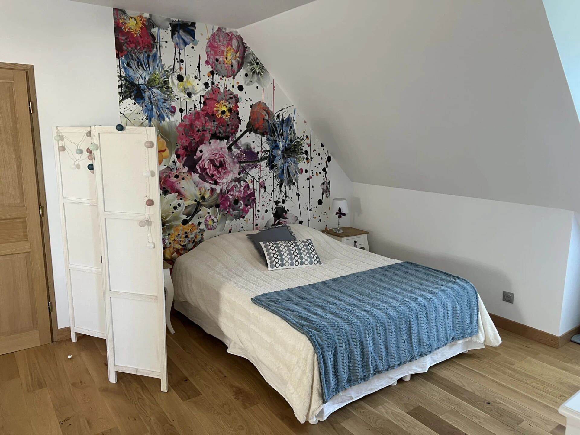 Une chambre à coucher avec un grand lit, une armoire, une table de chevet et une fresque murale à motifs floraux.