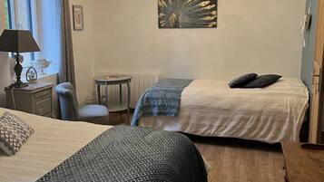 A bedroom with two beds, a chandelier, a painting, a small table, and a chair.