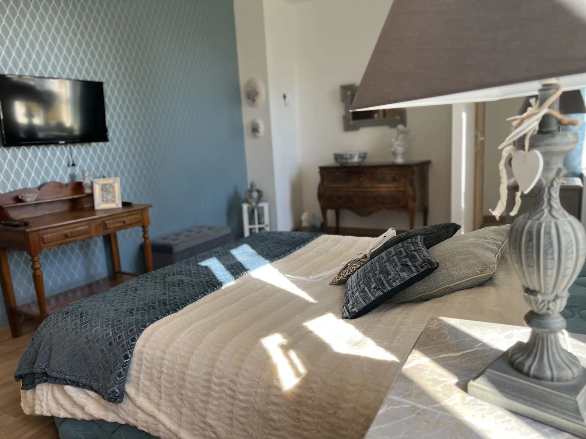A bedroom with a bed, a lamp, a TV, a dresser, and a small table.