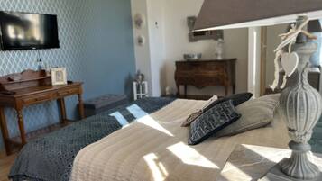 A bedroom with a bed, a lamp, a TV, a dresser, and a small table.