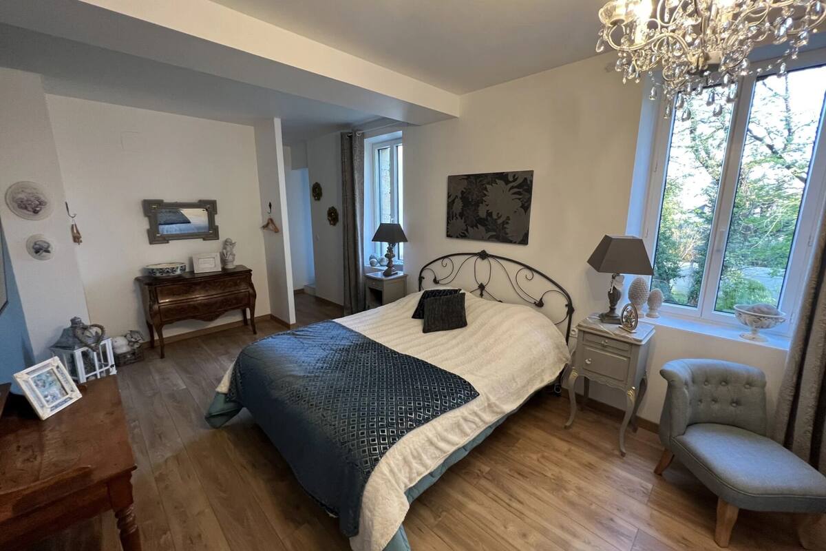 A bedroom with a large bed, a chandelier, a window with a view, a dresser, and a chair.