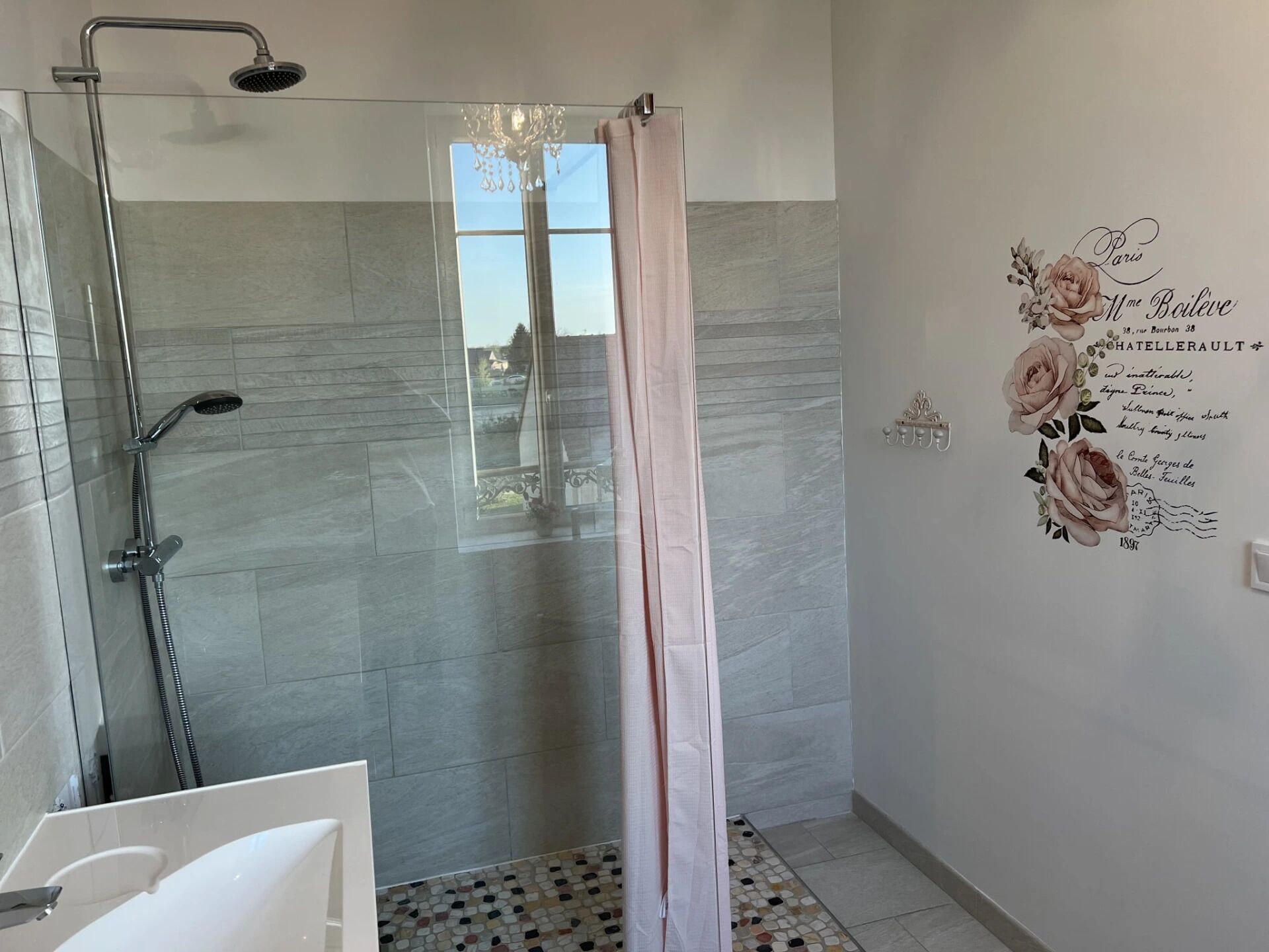 Une salle de bain moderne avec une douche à parois de verre, une baignoire blanche et un mur décoratif orné de motifs floraux.