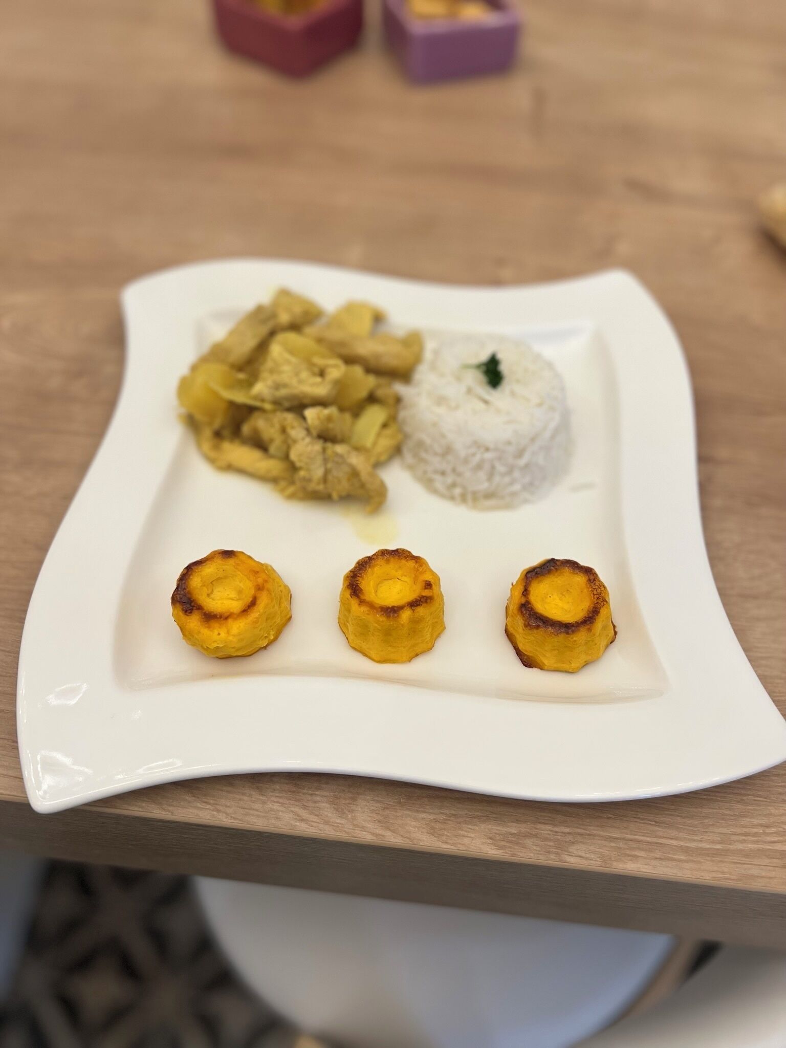 Un plato blanco con arroz blanco, pollo frito y tres plátanos fritos sobre una mesa de madera.