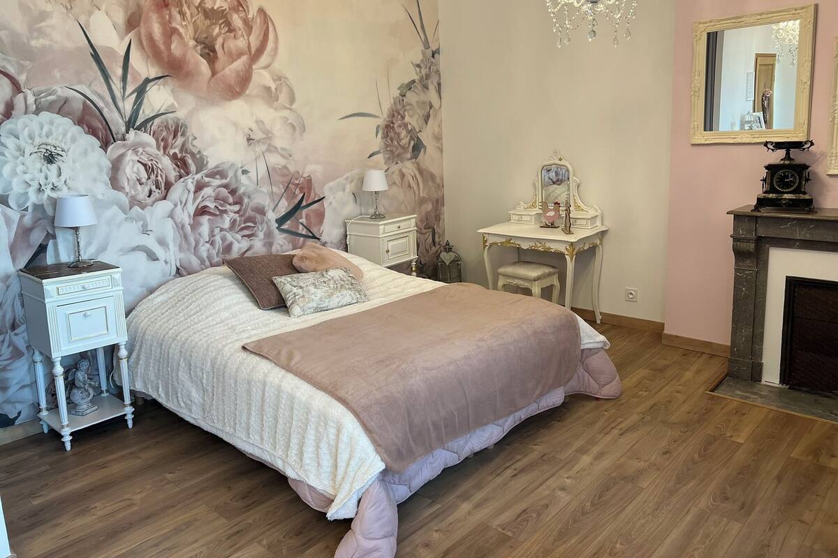 A bedroom with a large bed, a vanity with a mirror, a dresser, and a chandelier.