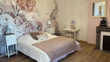 A bedroom with a large bed, a vanity with a mirror, a dresser, and a chandelier.