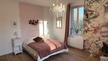 Een slaapkamer met een bed, nachtkastjes, een kroonluchter, een raam met gordijnen en bloemenbehang.