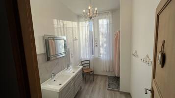 Een moderne badkamer met een dubbele wastafel, een spiegel, een kroonluchter en een douchehoek.
