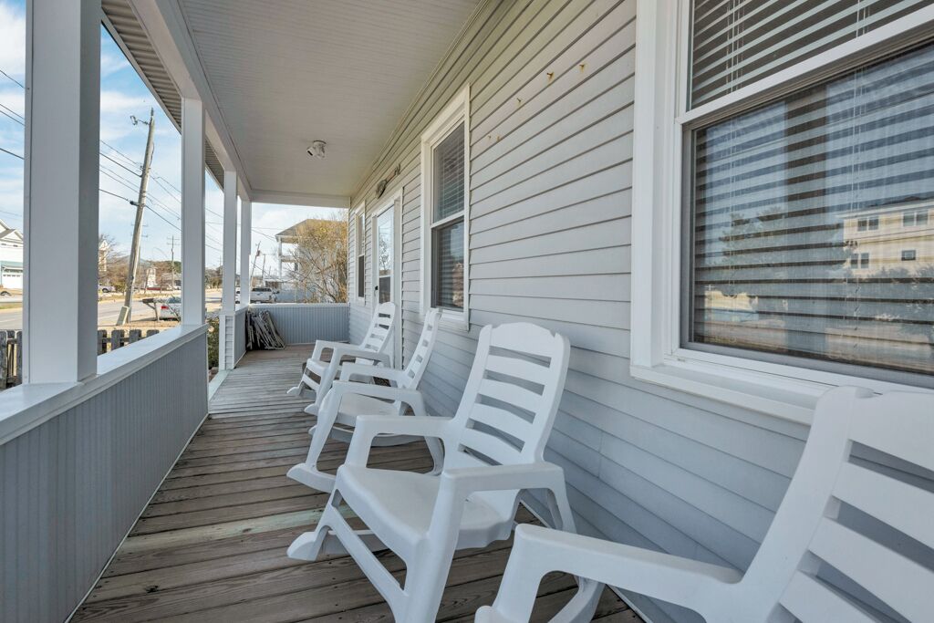 A covered porch with white plastic chairs and a wooden deck.