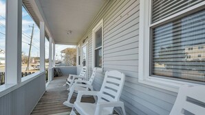 Une véranda avec des chaises en plastique blanc et une terrasse en bois.