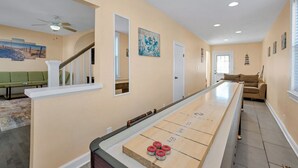Un grand salon comprenant une table de jeu de palet, un escalier et un canapé vert.