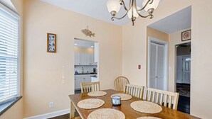 Une salle à manger avec une table en bois, des sets de table en fibres tressées et un lustre.