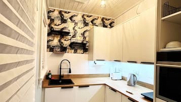 A compact kitchen with white cabinets, a marble backsplash, and a built-in oven.