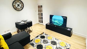 A living room with a black sofa, a yellow pillow, a black coffee table, a black TV stand with a TV displaying a travel channel, and a patterned rug.