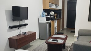 A modern living room with a flat-screen TV, a wooden cabinet, a refrigerator, a coffee table, and a sofa.