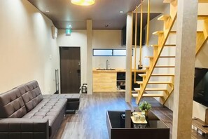 A modern living area with a sofa, a coffee table, a TV, and a staircase. - Tachibana (Osaka)