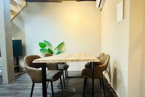 A dining area with a wooden table and four chairs, a plant, and a staircase in the background. - Tachibana (Osaka)