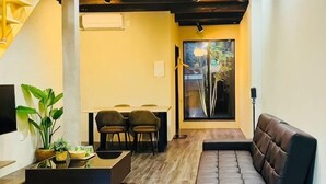 A modern living room with a sofa, a coffee table, and two chairs. There is a dining area with a table and chairs, and a large window providing a view of the outdoors. - Tachibana (Osaka)