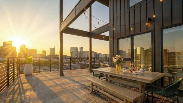An outdoor terrace with a dining table and chairs, a potted plant, and a city skyline view. - Downtown Nashville Penthouse|Huge Skyline Balcony (Nashville)