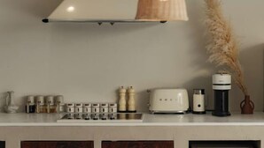 Une cuisine avec un plan de travail blanc, un grille-pain blanc, une machine à café et un vase contenant des plantes séchées.