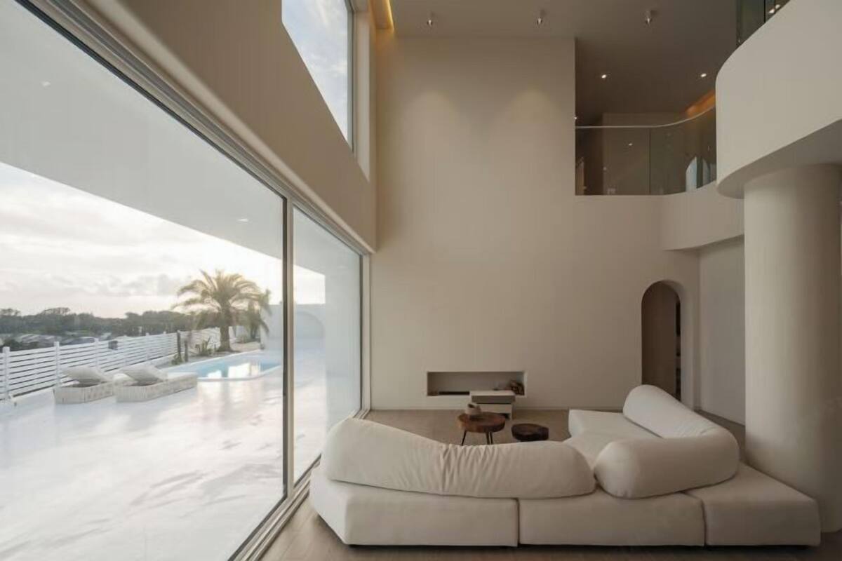 Una sala de estar moderna con un ventanal grande, un sofá blanco y una mesita.