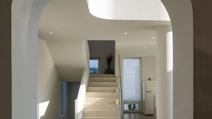 Un intérieur moderne avec un escalier menant à un deuxième étage, une porte dotée d’un panneau en verre dépoli et une petite table surmontée d’un vase.