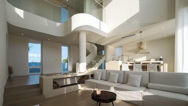 Un vaste espace de vie au design moderne, comprenant un grand canapé, une table basse et un escalier menant à un niveau supérieur.