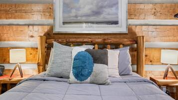 Una cama con colcha gris, cabecera de madera y un cuadro enmarco con un paisaje.