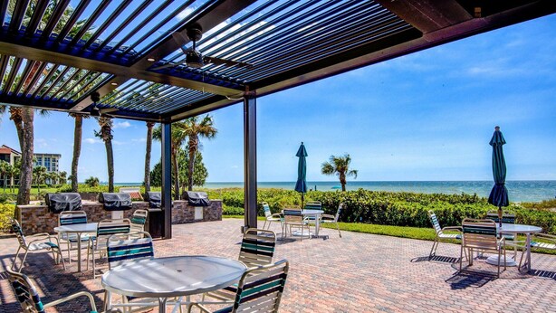 Une terrasse extérieure avec des tables et des chaises, un espace abrité et une vue sur l’océan.