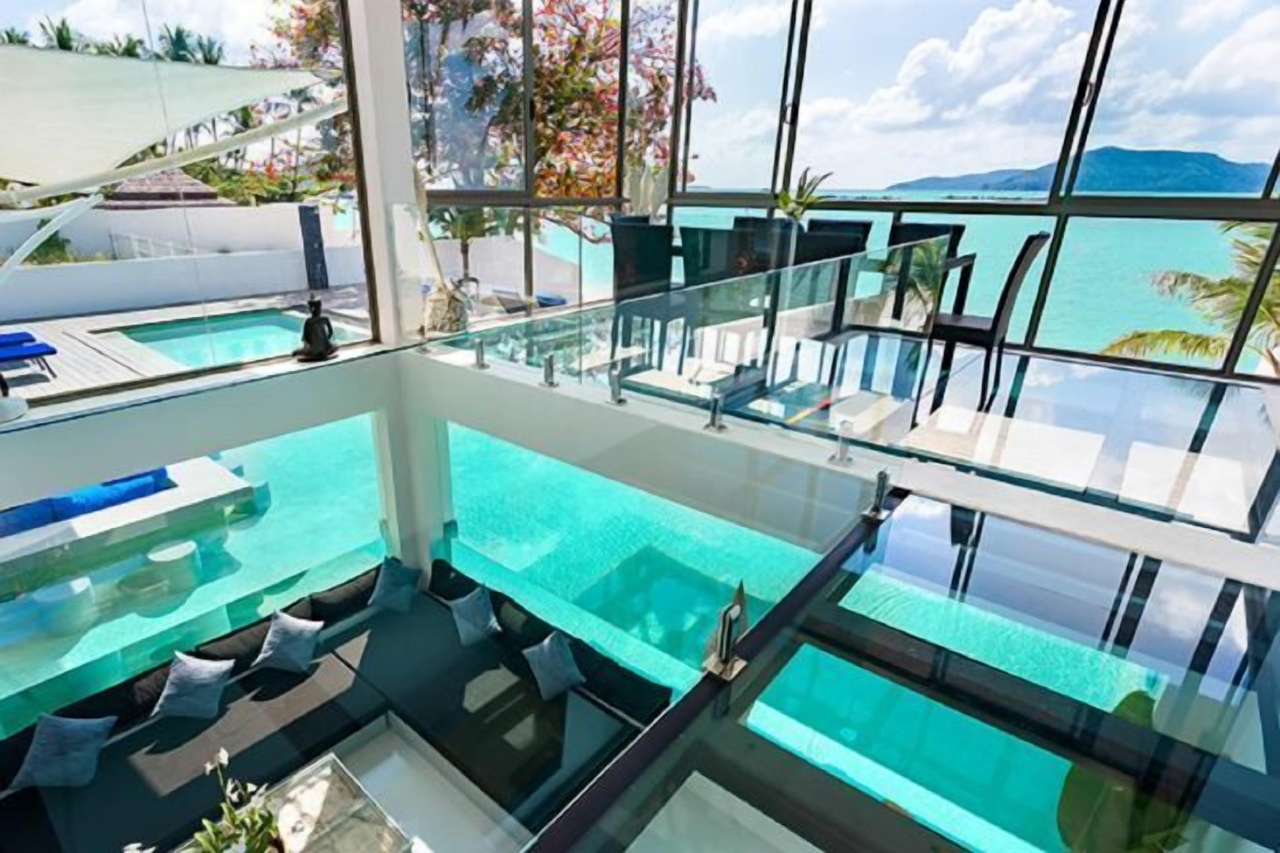 A modern indoor pool with glass walls, offering a view of the ocean and mountains.