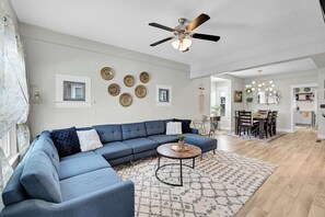 A modern living room with a sectional sofa, a coffee table, and a dining area with a chandelier.