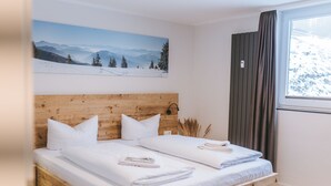 A double bed with wooden headboard, white bedding, and a mountain landscape painting above it. - Vacation apartment Schneeglück for 10 people with large terrace (Winterberg)