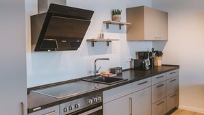 A modern kitchen with a built-in stove, oven, and a range hood. There are cabinets, a sink, and a countertop with a coffee maker and utensils. - Vacation apartment Schneeglück for 10 people with large terrace (Winterberg)