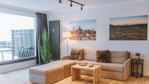 A modern living room with a sofa, a wooden coffee table, and a large window with curtains. - Vacation apartment Schneeglück for 10 people with large terrace (Winterberg)