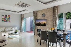 A modern living room with a sofa, coffee table, and dining area with chairs and a table. - Trixie Town House Unit 2 (Phuket)