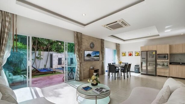 Een moderne woonkamer met een glazen deur naar een terras, een eethoek en een keuken met roestvrijstalen apparatuur.