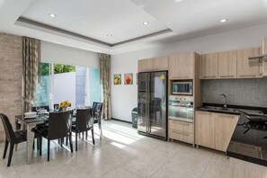 A modern kitchen with a dining area, featuring a refrigerator, microwave, and stove. - Trixie Town House Unit 2 (Phuket)