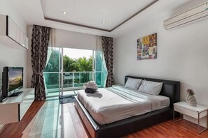 A modern bedroom with a large bed, a television, and a window with curtains. - Trixie Town House Unit 2 (Phuket)