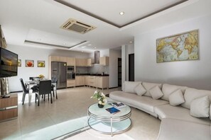 A modern living room with a sofa, coffee table, and dining area. - Trixie Town House Unit 2 (Phuket)