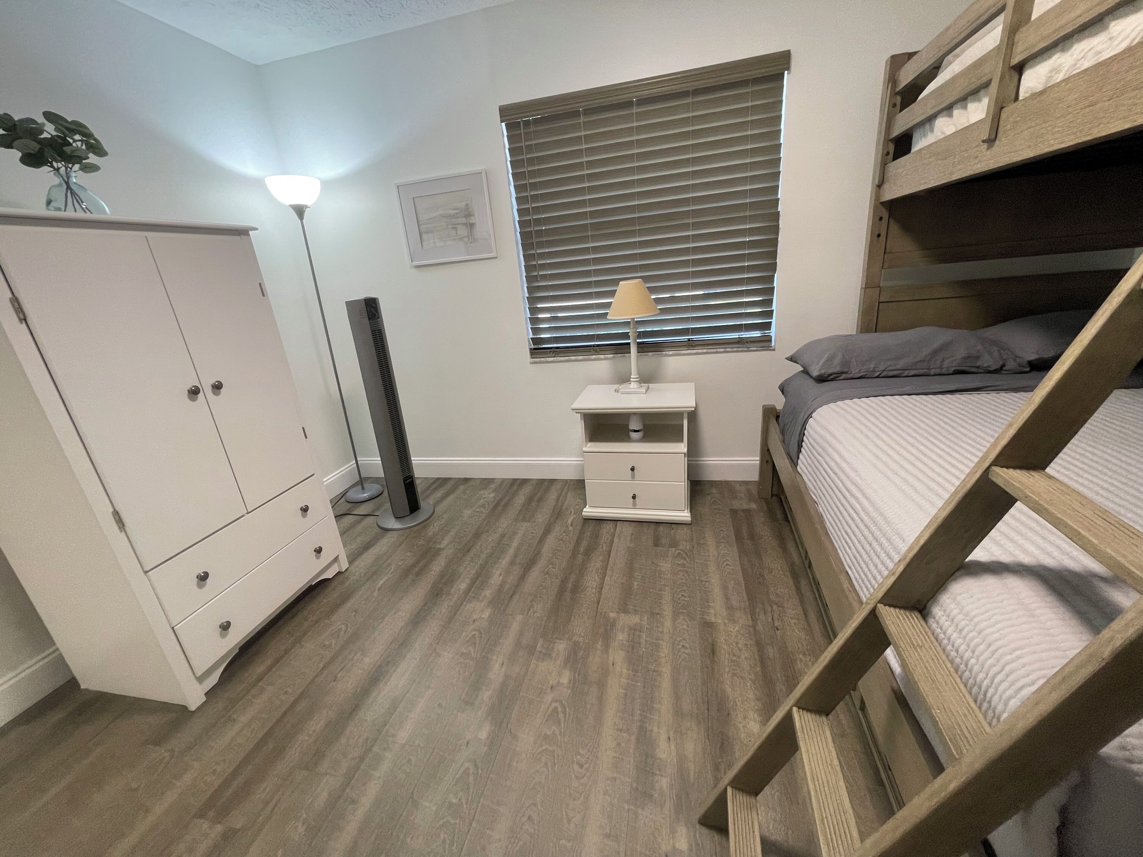 Una camera da letto con un letto a castello, un comodino con una lampada, un armadio e una finestra con persiane.