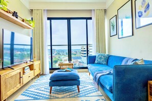 Un salon moderne doté d’une grande fenêtre, d’un téléviseur à écran plat, d’un canapé bleu et d’un meuble en bois.