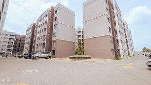 Un immeuble résidentiel à plusieurs étages, doté d’un espace paysager central, de places de stationnement et offrant une vue dégagée sur le ciel.