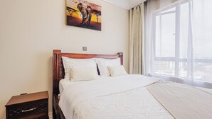 Une chambre d’hôtel avec un grand lit, une tête de lit en bois, une table de chevet et un tableau représentant un éléphant accroché au mur.