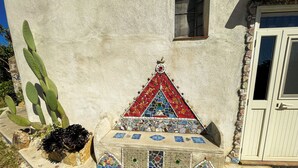A building with a textured exterior, a small triangular mosaic decoration, and a door with a stone border. - [Casa dolce sole]  Holiday Home in Sciacca - Comfort and Relax Near the Sea! (SCIACCA)