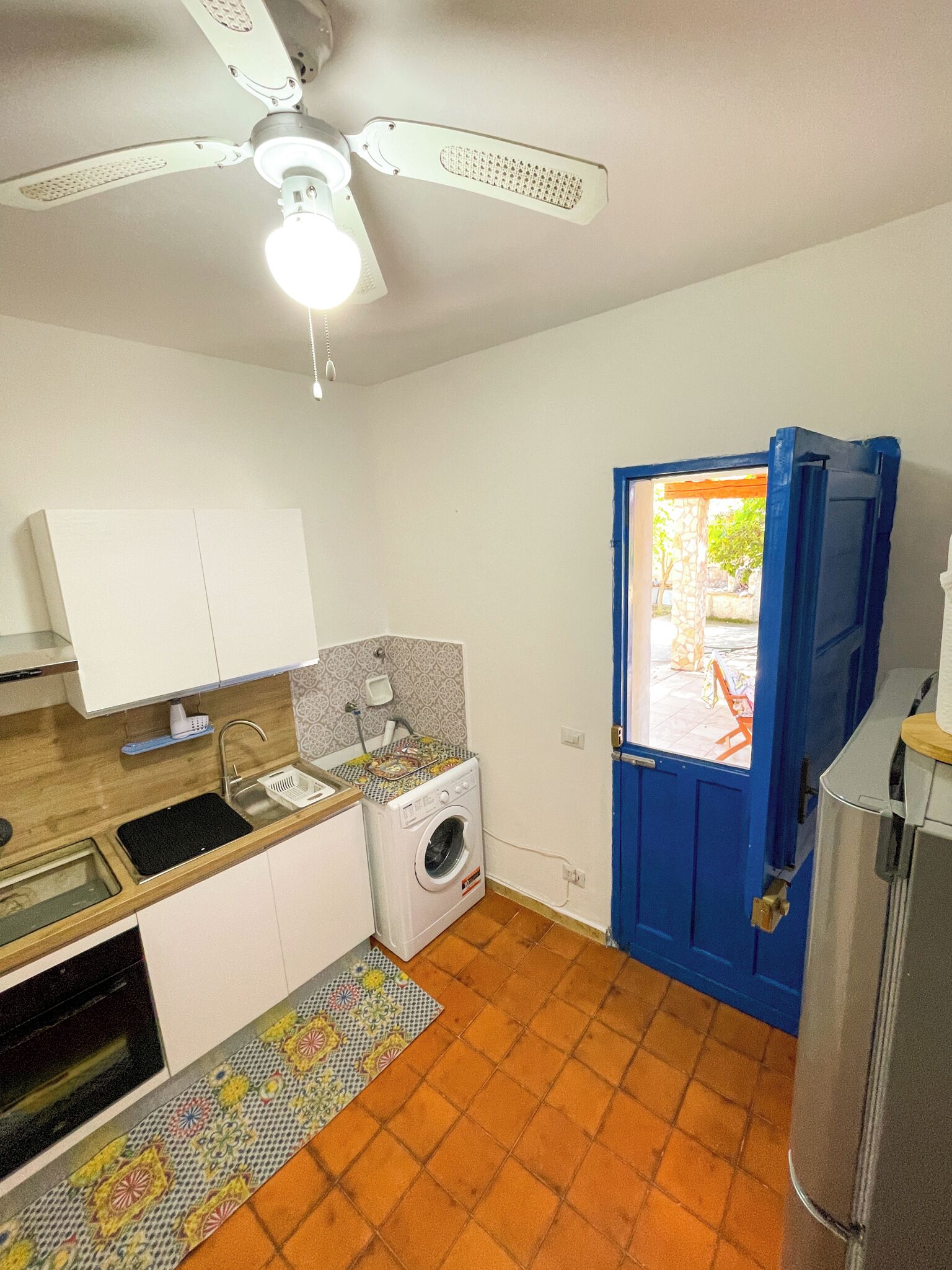Een kleine keuken met een wasmachine, een spoelbak en een plafondventilator.