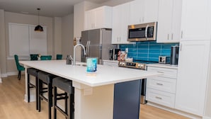 Une cuisine moderne avec des meubles blancs, un îlot central et un pare-feu bleu.