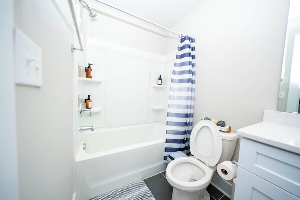A modern bathroom with a bathtub, toilet, and shower curtain. - Modern Home near Plaza Midwood (Charlotte)