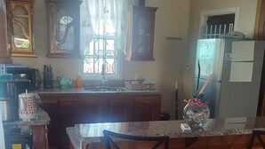 A kitchen with wooden cabinets, a central island with bar stools, a refrigerator, and a window with curtains.