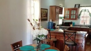 A dining area with a wooden table and chairs, a vase with flowers, and a kitchen in the background.