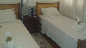 A hotel room with two beds, a nightstand with a lamp, and a window with curtains.