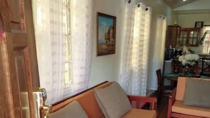 A room with a wooden sofa, a dining table with chairs, and a patterned rug.